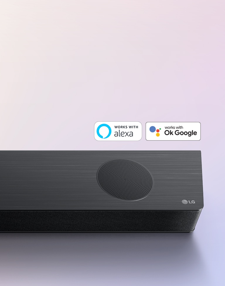 A Sound Bar LG está colocada no chão, tendo o logotipo LG no canto direito. Os logotipos Alexa e OK GOOGLE estão dispostos acima da sound bar.