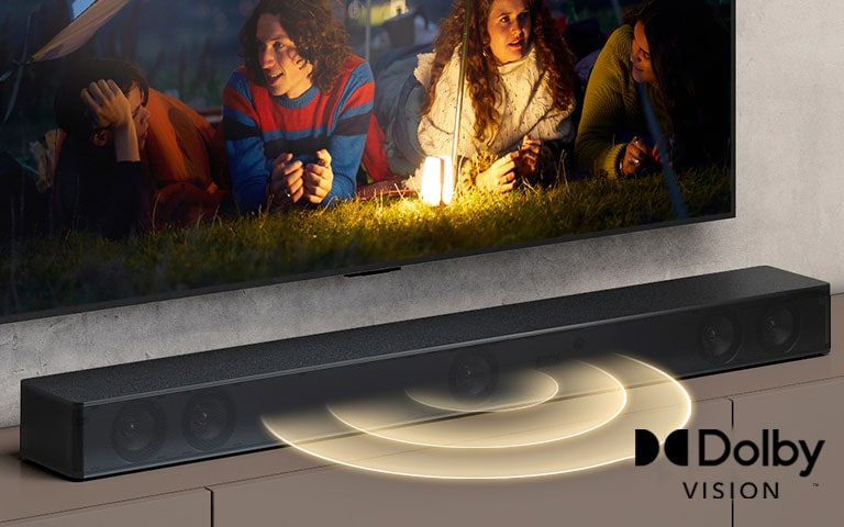 A TV LG está na parede, e sua tela mostra dois casais deitados na grama. Na frente deles, há um lampião. A Sound Bar LG está abaixo da TV LG. Ondas sonoras são emanadas na frente da sound bar. O logotipo DTS Virtual:X logo aparece no canto inferior direito da imagem.