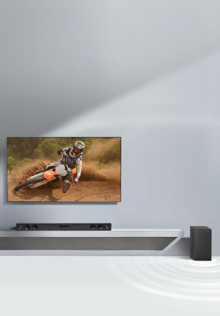 Sound Bar LG SQC2 e TV LG estão dispostas juntas numa sala de estar. O subwoofer está colocado ao lado da barra de som. A TV está ligada, exibindo a imagem de uma motocicleta.