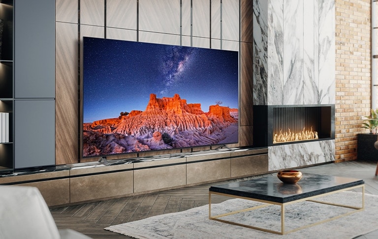 Em um quarto simples com vista para o mar, há uma TV em uma prateleira de parede. A paisagem azul do mar aparece brilhante e clara na tela da TV.