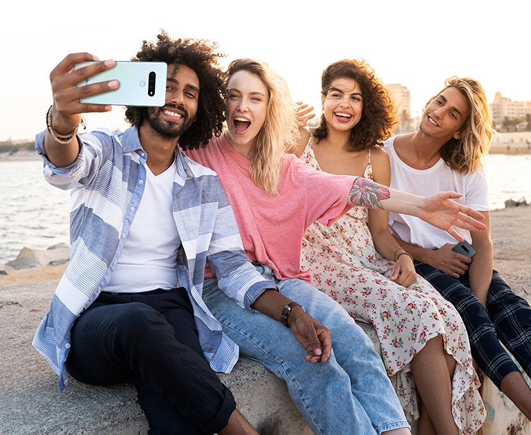 Quatro pessoas sentadas na praia tirando selfies.