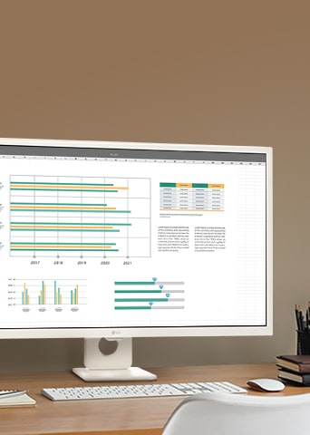  Monitor LG exibe gráficos coloridos sobre uma mesa com teclado, mouse e canetas organizados ao lado.