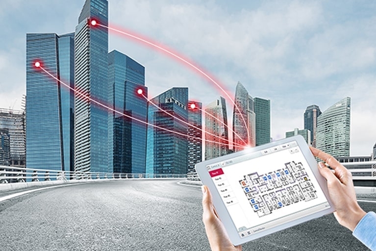 Uma pessoa segura um tablet exibindo uma solução de controle. Quatro linhas vermelhas se estendem do tablet, conectando-se aos edifícios à esquerda.