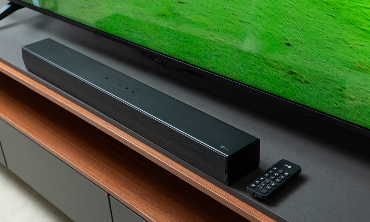 Uma soundbar da LG e um controle remoto posicionados em frente a uma TV LG QNED