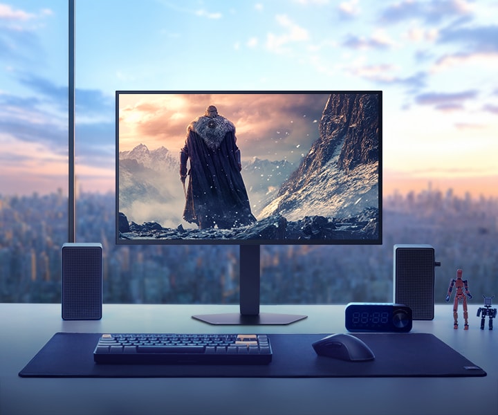 Monitor LG UltraGear 27GX790B colocado sobre uma mesa com vista para a paisagem urbana ao pôr do sol, exibindo uma cena de jogo de fantasia com um personagem de capa em um ambiente de montanha coberta de neve. Ao redor do monitor há alto-falantes, um teclado, um relógio, pequenas figuras e uma caneca.