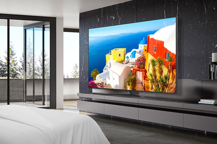 A TV is installed on a stand close to the wall in the hotel room, and the screen is bright and clear.