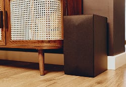 Wireless subwoofer placed next to a wooden cabinet in a living room