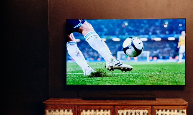 Large TV showing a soccer match above a wooden TV stand in a cozy living room.