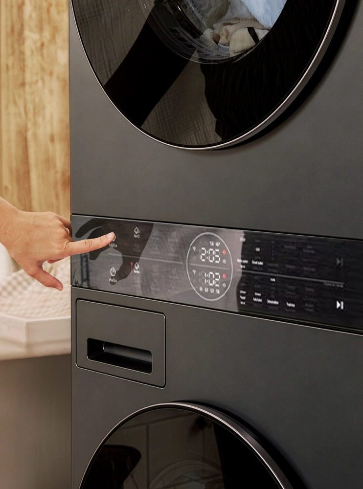 A close-up of a hand pressing a button on the center control panel of a stacked washer and dryer unit.