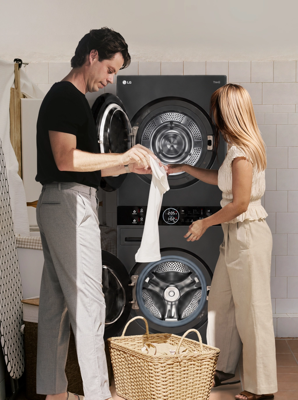 A man and woman transferring laundry between a stacked washer and dryer in a laundry room.