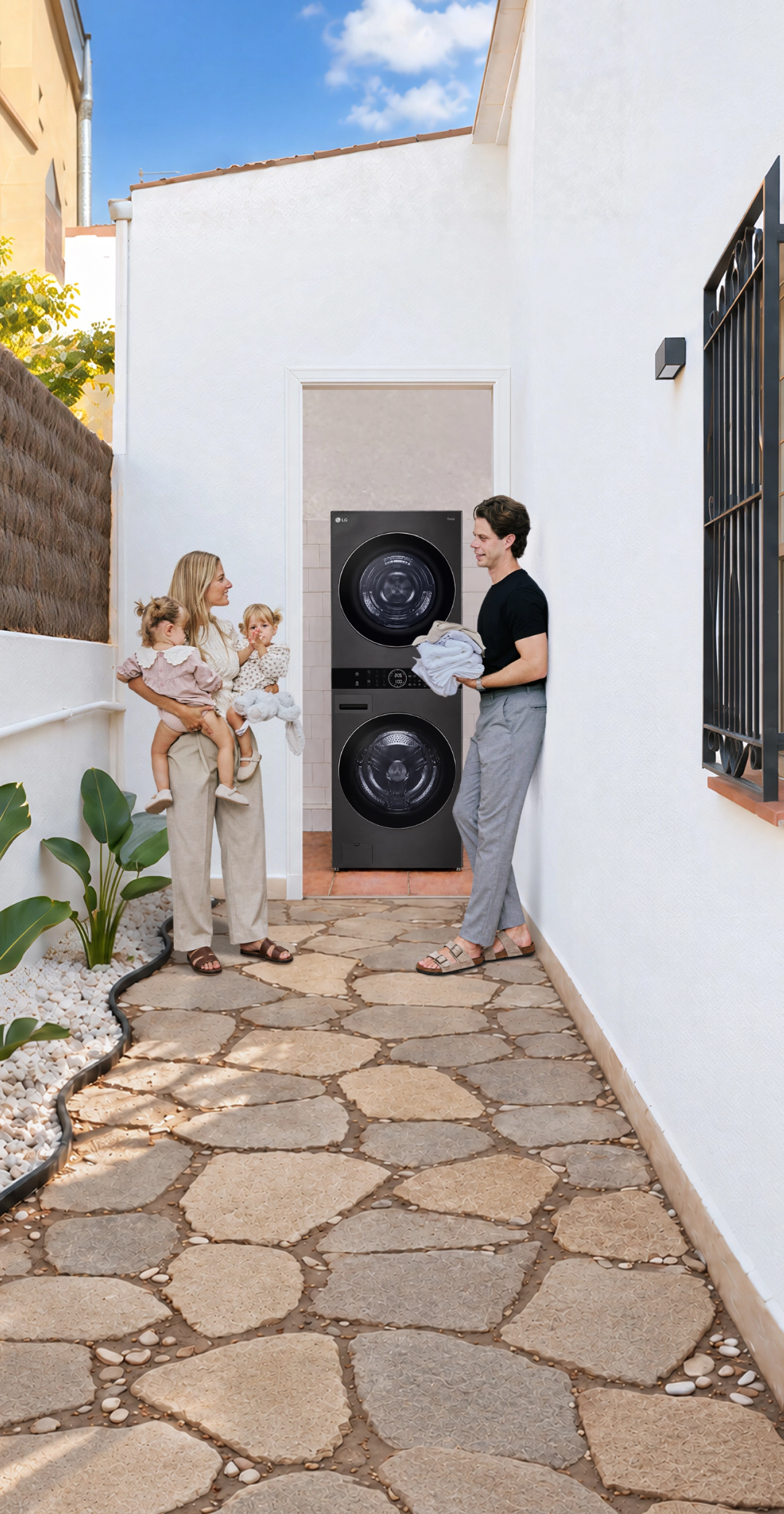 A family with toddler twins standing in a white-walled outdoor hallway next to a stacked LG washer and dryer unit.