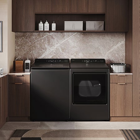 The LG Top Load Washer and Dryer set (WT8405CB) in Black Steel, showcasing its premium, side-by-side design seamlessly integrated into a luxurious laundry room with marble and wood finishes.