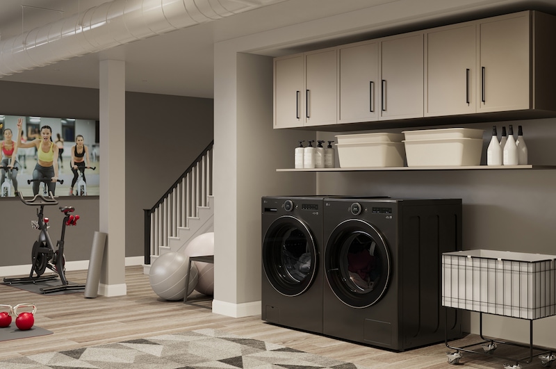 The LG Front Load Washer and Dryer set (DLHC6702B) in Black Steel, showcasing its premium aesthetic and seamless integration into a modern, multi-purpose utility and gym space.