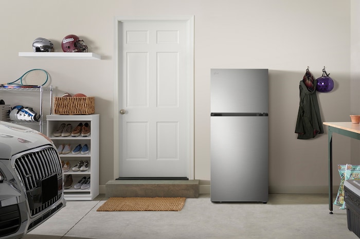The stainless steel finish LG 28-inch 18 cu.ft. Top Freezer Refrigerator LT18S2100S, shown placed in a garage setting.