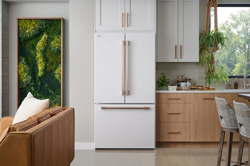 The white finish LG STUDIO 36-inch 27 cu.ft. French Door Refrigerator SRFB27W3 with bronze handles, installed in a warm-toned modern kitchen.