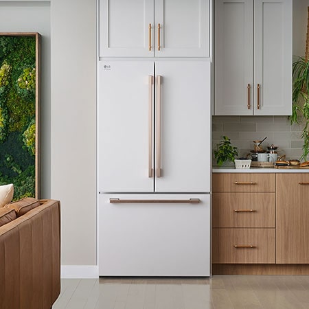 The white finish LG STUDIO 36-inch 27 cu.ft. French Door Refrigerator SRFB27W3 with bronze handles, installed in a warm-toned modern kitchen.
