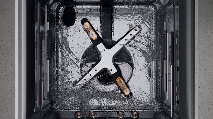 Close-up view inside an LG dishwasher showing the lower spray arm and stainless steel tub during a wash cycle, with water spraying across the interior for thorough cleaning.