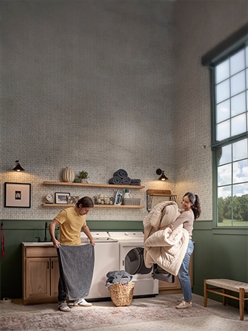 A cheerful couple does laundry together using their LG top load washer and dryer in a bright, stylish laundry room. They’re smiling while folding towels and unloading a comforter, showing how easy and enjoyable laundry can be with reliable LG appliances—ideal for illustrating LG service and support.