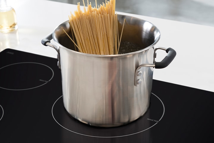 Stainless steel pot with boiling water on a black glass induction cooktop with a glowing red heating element.