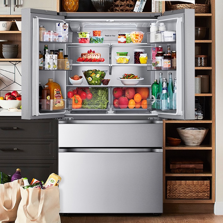 Open stainless steel French door refrigerator filled with fresh food, highlighting the spacious interior and air filter.