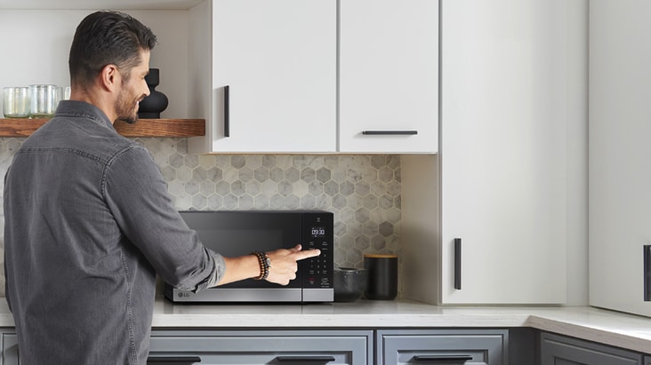 A man using the touch control panel of a black and silver LG countertop microwave in a modern kitchen.
