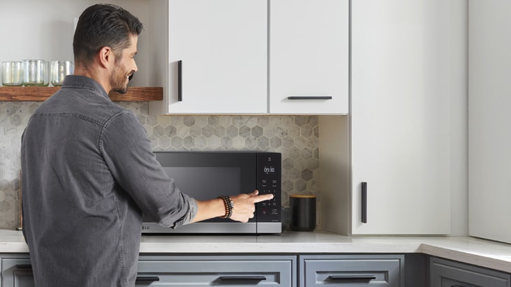 A man using the touch control panel of a black and stainless steel LG countertop microwave in a modern kitchen.