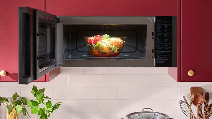 Stainless steel over-the-range microwave installed flush against a white cabinet, showing the zero-clearance door open.