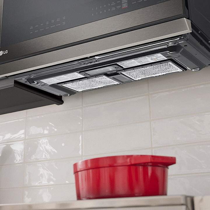 Underside of an LG over-the-range microwave showing the mesh grease filters and vent system above a stove.