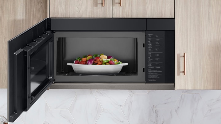 Open black built-in microwave containing a white dish filled with steamed mixed vegetables.
