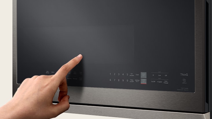 A person's finger touching the glass control panel of a black stainless steel microwave with digital touch buttons.