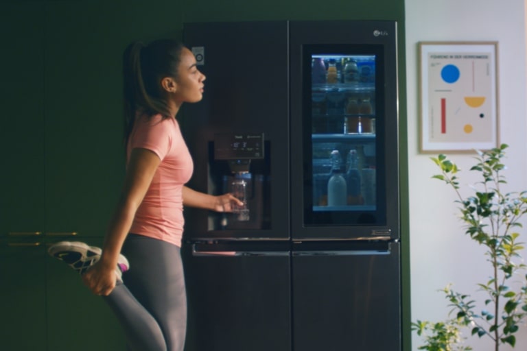 Woman getting filtered water from refrigerator water dispenser after work out