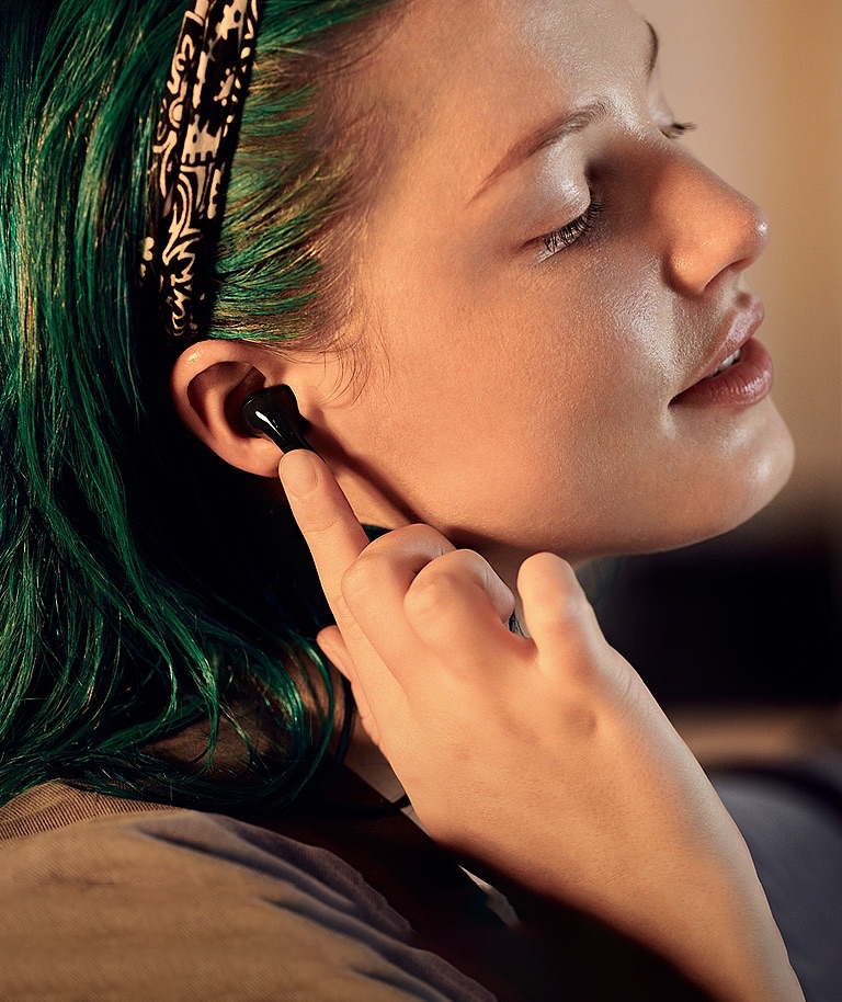 A woman seen in profile. She is wearing T60 earbuds and tapping on one with her finger.