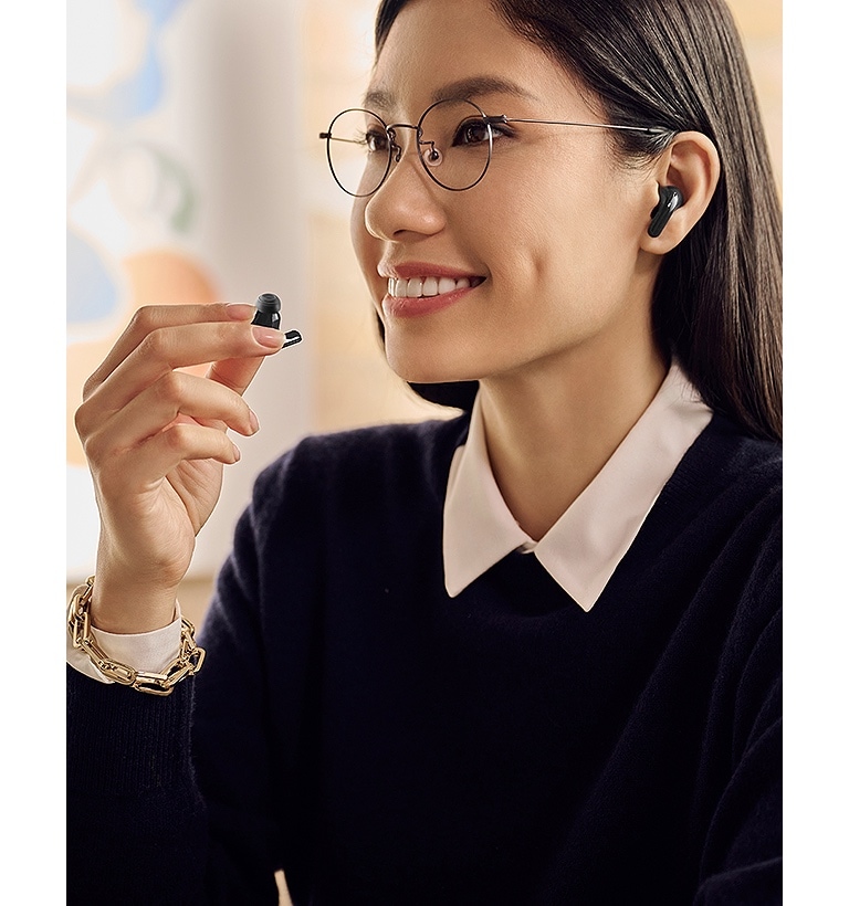 A woman is using the earbuds and holding one in her right hand while whispering into it.