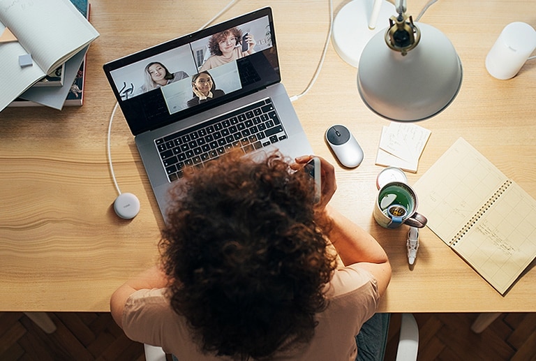 A woman is working on a computer and uses Plug and Wireless to participate in a conference call.