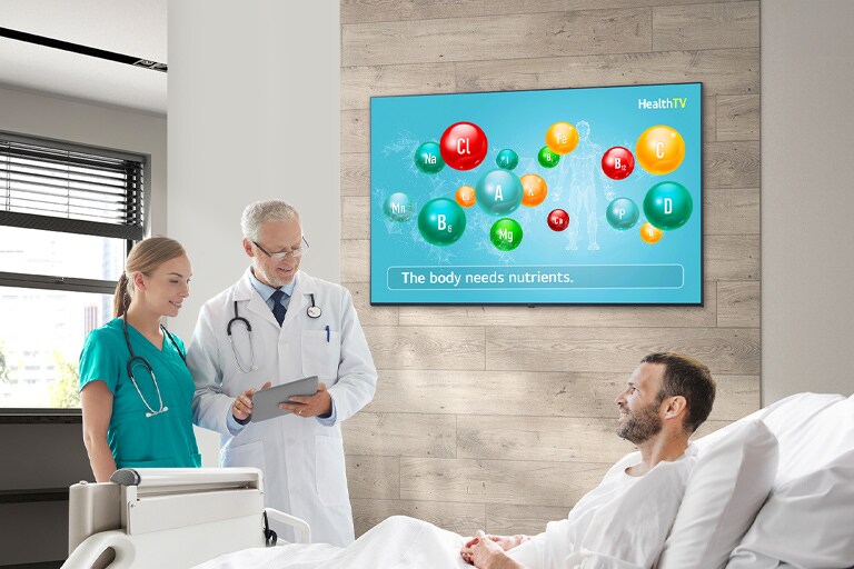 A doctor and a nurse are visiting a patient resting in a hospital room, and the UM672M is hung on the wall next to them.
