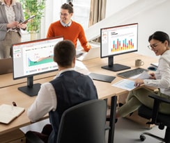 Employees sitting at office desks and having a conversation.	