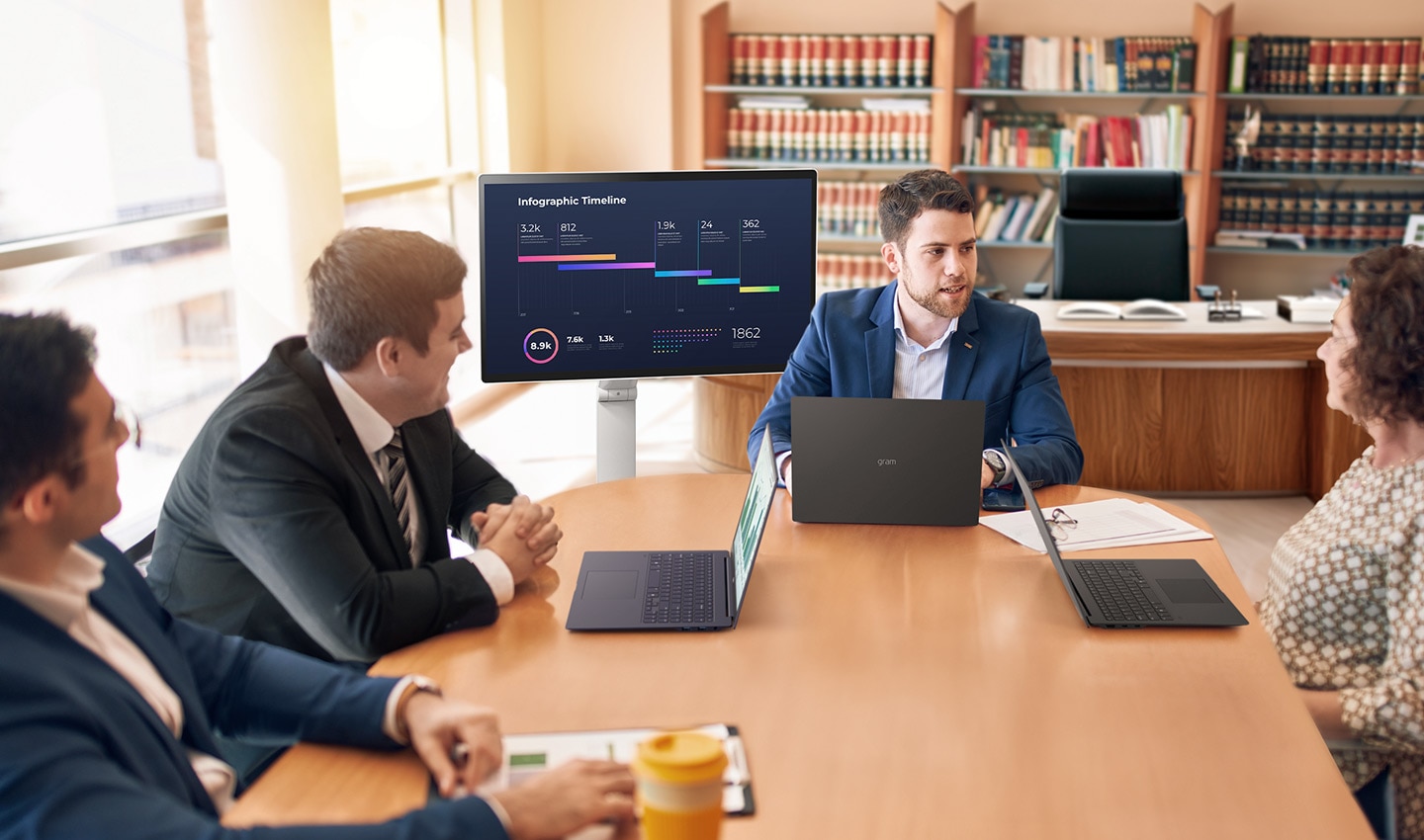 Four people are sitting around a desk, having a meeting using a LG Smart Monitor Swing.