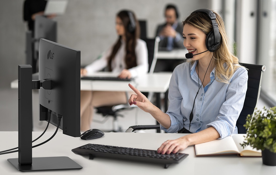 A woman is wearing a headset and working while looking at a monitor.