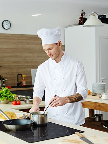 Professional chef cooking with a pot on a sleek black induction cooktop in a modern kitchen, highlighting the precision and efficiency of induction technology.