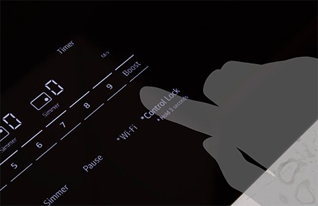 Hand activating the control lock on an LG induction cooktop, which prevents accidental use and provides added safety for households with children.