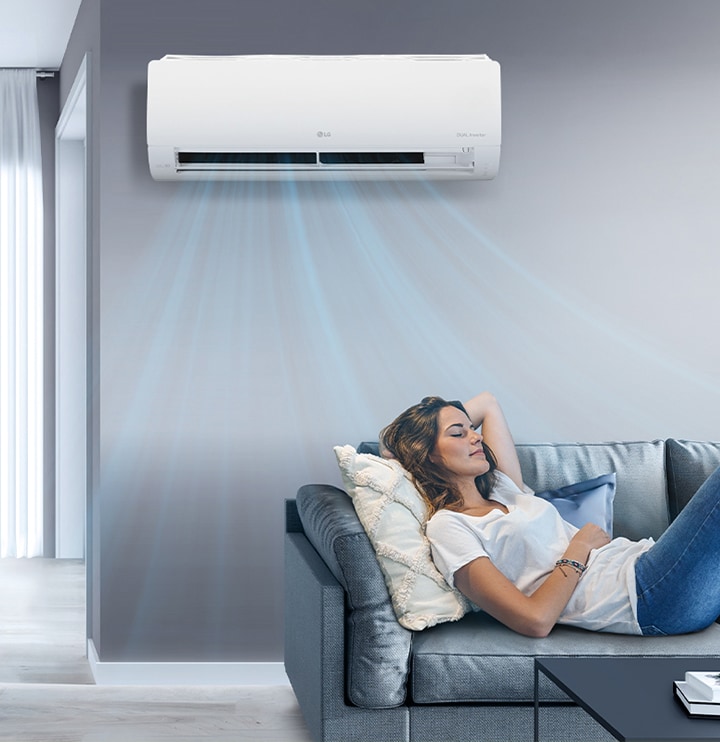 A woman lounges on a couch in a living room with the LG air conditioner installed above her on the wall. Blue streams of air are on the image to indicate it is on and cooling the room.