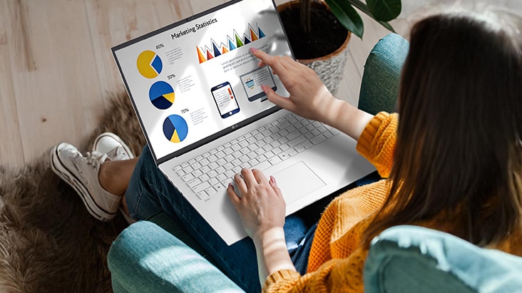 A person sitting comfortably in a chair, using a laptop that displays a presentation with charts and graphs. An animation demonstrates the anti-glare screen by showing no light reflection even when sunlight shines directly onto the display.