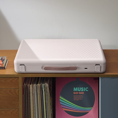 StanbyME Go is placed on top the wooden shelf filled with LPs. The screen is closed, showing the strap.