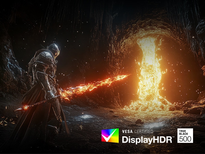 A heavily armored warrior stands in a dark, rocky cavern wielding a glowing, fiery sword. In front of the warrior, a massive torrent of molten lava pours down from the cave ceiling, casting a bright, intense orange light across the scene. The contrast between the darkness of the cave and the blazing fire emphasizes the game's dramatic and cinematic visual style.