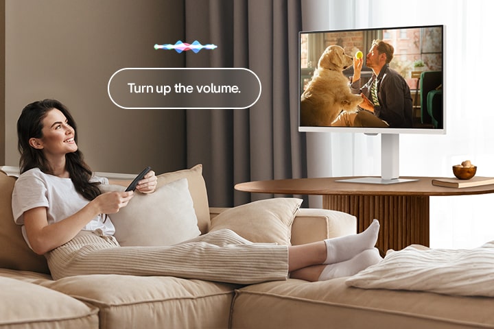 A woman is turning up the LG Smart Monitor’s volume using a Magic Remote.