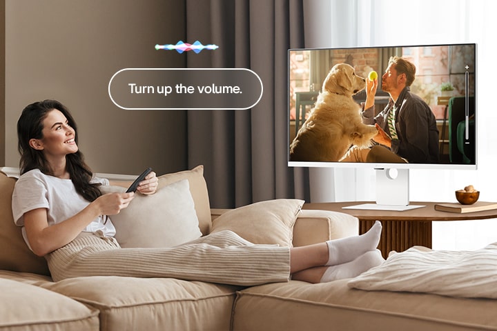 A woman is turning up the LG Smart Monitor’s volume using a Magic Remote.	
