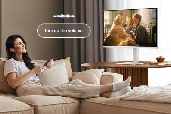A woman is turning up the LG Smart Monitor’s volume using a Magic Remote.