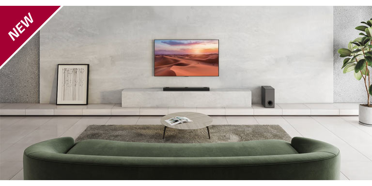 TV is hung on the white pillar in the center of the living room. Below, LG Sound Bar is placed on the white shelf. On the floor right under the sound bar, a wireless subwoofer stands. Behind the green sofa, two rear speakers are placed on the coffee table both the left and right sides. NEW mark is shown in the top left corner.