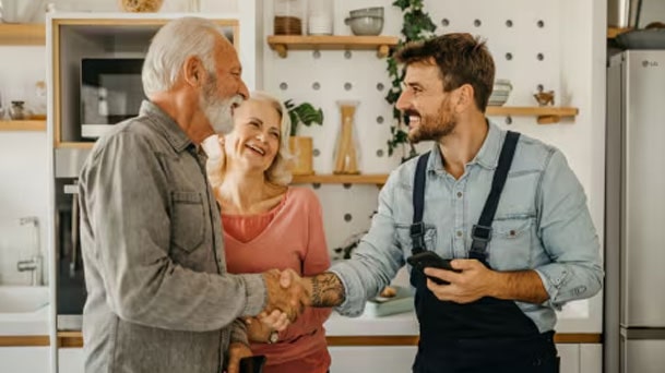 Smiling LG technician explains something to a customer inside a bright, modern kitchen, representing LG’s in-home service and flat-rate repair support.