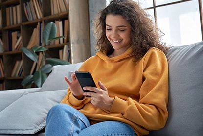 The image of a woman sitting on a sofa smiling and looking at her phone
